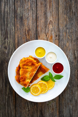 Crispy breaded seared chicken cutlet with lemon slices and fresh vegetables on wooden table
