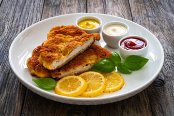 Crispy breaded seared chicken cutlet with lemon slices and fresh vegetables on wooden table
