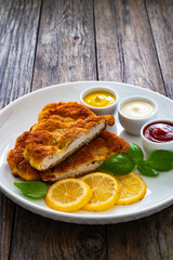 Crispy breaded seared chicken cutlet with lemon slices and fresh vegetables on wooden table
