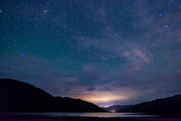 Fototapeta na wymiar starry sky above the shape of mountains with the light of a city in a fjord in the Marlborough Sounds, New Zealand 
