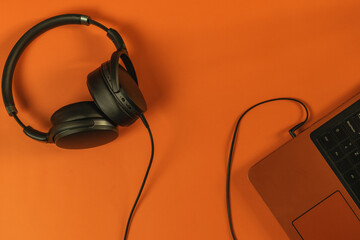 Black headphones connected to laptop on orange background