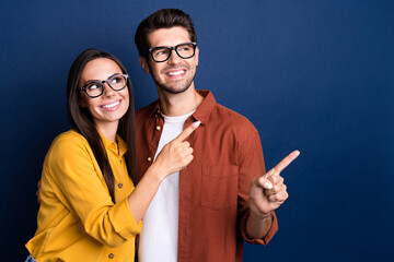 Portrait of successful positive partners beaming smile look direct finger empty space information isolated on blue color background