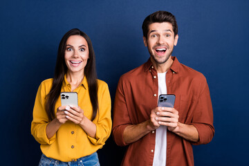 Portrait of two impressed funky people open mouth use smart phone facebook telegram isolated on...