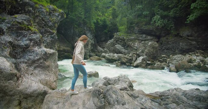 Active tourist woman walks along a rocky gorge with a fast-flowing deep river. Bright landscape in Alps. Girl enjoying nature in forest.