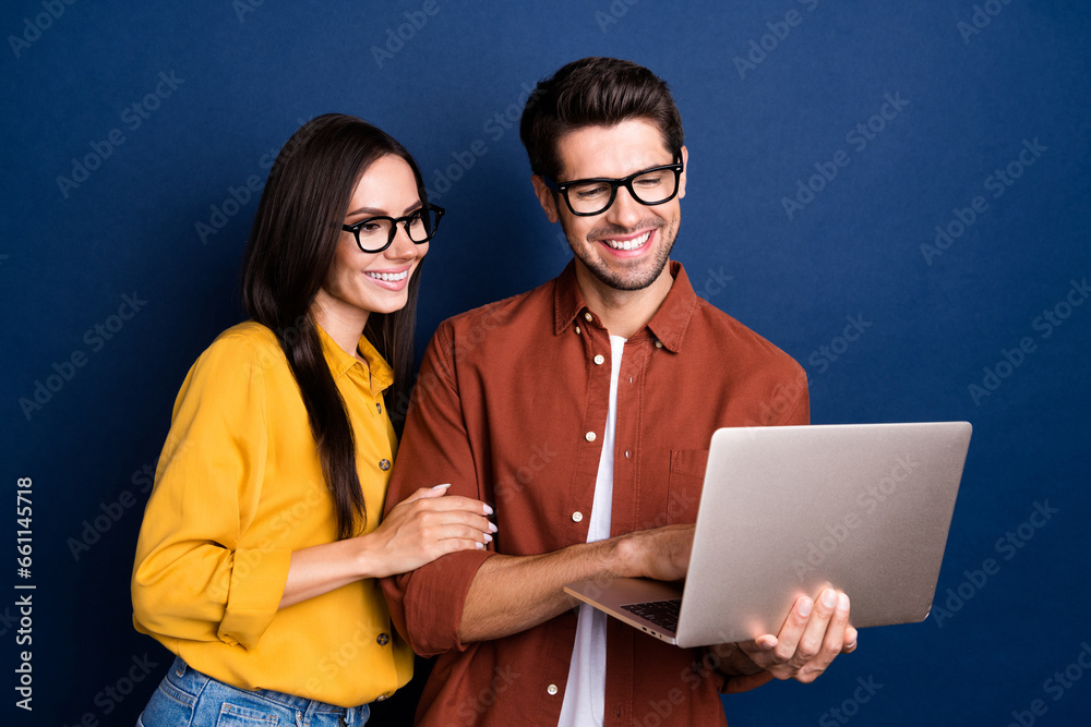 Poster portrait of two attractive positive colleagues use wireless netbook develop project isolated on blue