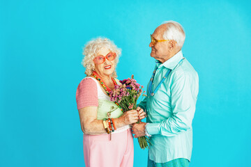 Beautiful senior old couple wearing fancy party clothes acting in studio on a colored background. Conceptual image about third age and seniority, old people feeling young inside.