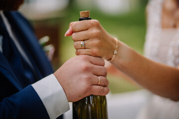 The groom and the bride hold a bottle with a letter in their hands while displaying their wedding rings, symbolizing their commitment and love in a heartfelt gesture