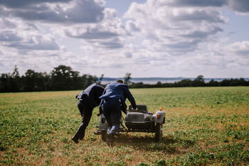 Two men are seen pushing a motorcycle with a sidecar, working together to navigate the vintage vehicle