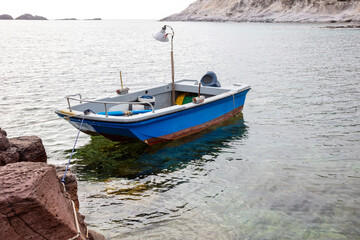 Naklejka na ściany i meble beautiful blue boat is moored to a rock