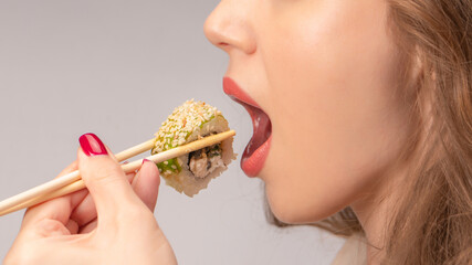 Young woman with red nails is eating sushi.