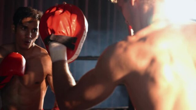 Asian and Caucasian Muay Thai boxer unleash punch in fierce boxing training session, delivering punching strike to sparring trainer, showcasing Muay Thai boxing technique and skill. Impetus