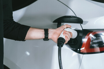 Young man travel with EV electric car to shopping center parking lot charging in downtown city...