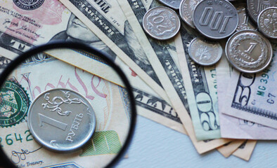 Ruble coin with a magnifying glass against background of dollars.