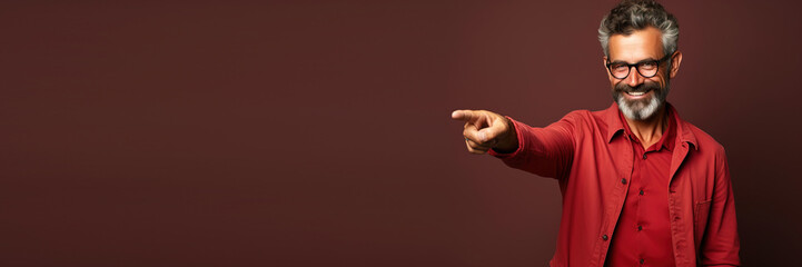 middle age man wearing red casual clothes pointing with hand and finger to the side against a red seamless background. Banner design with space for text