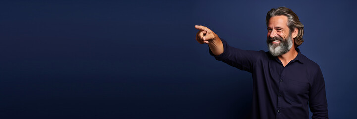 middle age man wearing a casual clothes pointing with hand and finger to the side looking to the side against a blue studio background. Banner design with space for text