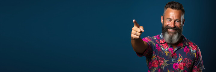 young bearded man wearing informal clothes pointing with hand and finger to the side looking at the camera against a violet background. Banner design with space for text