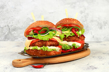 Two double cheeseburgers with fresh lettuce, tomato, cream cheese, cucumber, onion, chili pepper and cutlet on an old wooden board, food delivery concept, menu and advertising for cafe and restaurant