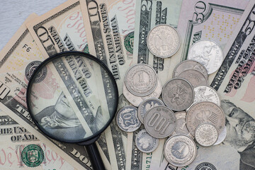 Magnifying glass, different metal coins on paper dollar bills, top view.