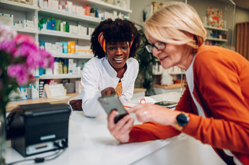 Senior woman showing smartphone screen to an african american female pharmacist