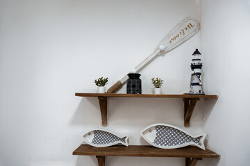 decorative fish, lighthouse and plants against white wall on wooden shelves form nautical seaside...