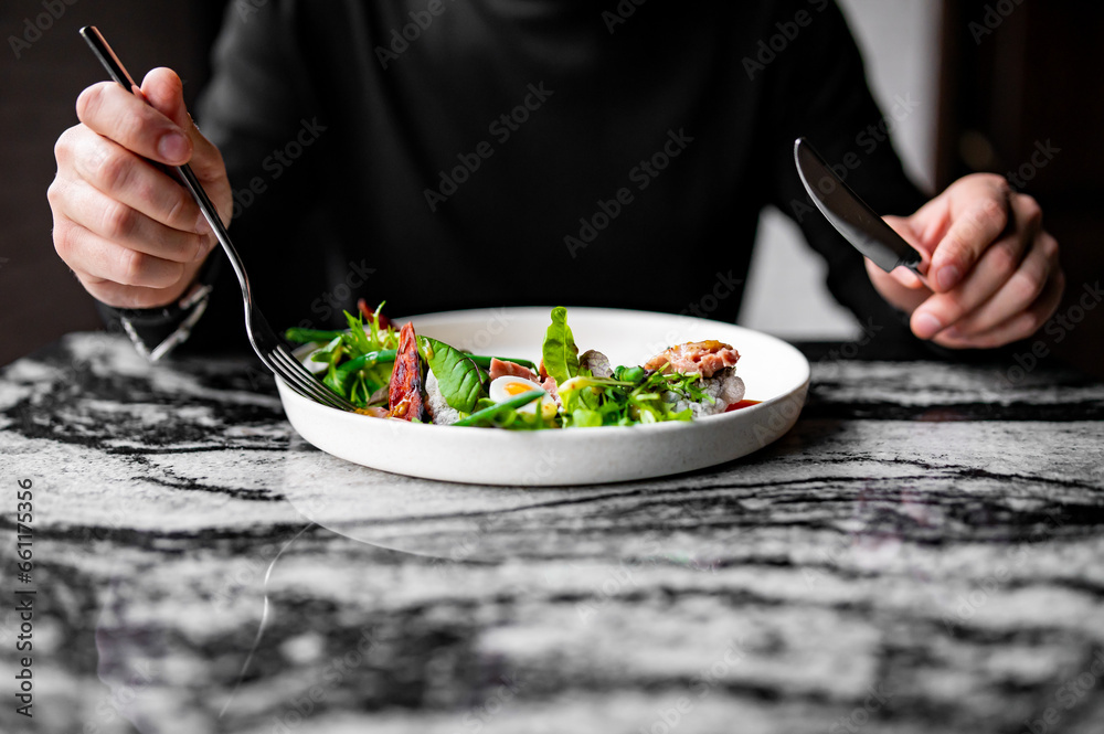 Wall mural hands of a man with a fork and knife eat salad nicoise. tuna, with green beans, tomatoes, potatoes a