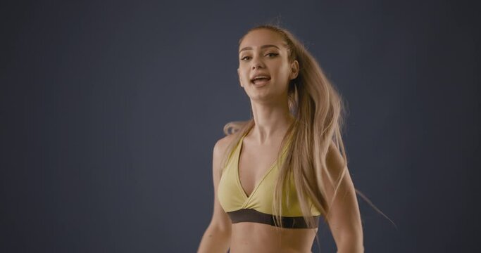 Beautiful blond girl in black outfit dancing zumba against smoke fog and blue background.