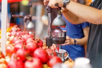 A fresh juice seller on the street squeezes juice from a pomegranate.