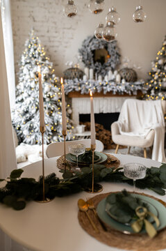 A decorated table with exquisite candles, plates and glasses. New Year or Christmas style. Bokeh from a Christmas tree in the background.