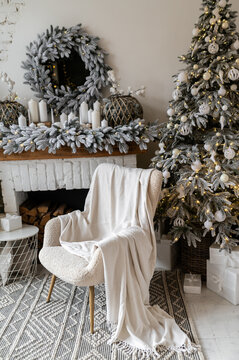 A soft chair covered with a plaid against the background of a New Year's fireplace decorated with Christmas trees, lights and candles