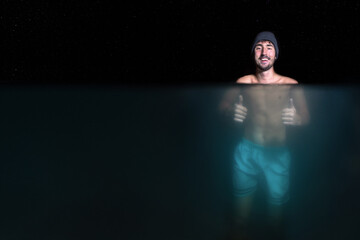 smiling man doing bath in cold water showing thumbs up under water view under the stars at night