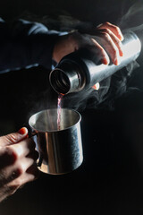Pouring hot tea from thermos bottle to steel cup in the dark