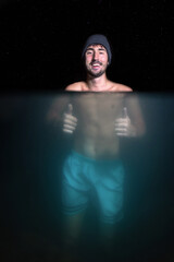 smiling man doing bath in cold water showing thumbs up under water view under the stars at night