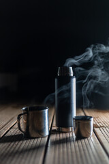steaming hot tea in flask and cups in the dark on wooden floor