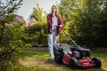 Female gardener working in autumn, cutting grass in backyard. Concept of gardening, work, nature. Housework, gardening and country life. Home garden grass cutting woman mowing with lawn mower.