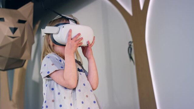 Adorable toddler girl with a virtual reality headset standing in a natural history museum playroom, low angle shot. Concept of children and modern technologies.
