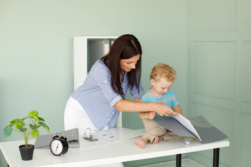 Fototapeta premium Beautiful business lady holding her cute little baby, and smiling while working in office