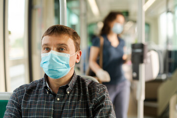Adult man wearing medical mask and rubber gloves riding city bus on way to work in sunny spring morning. Individual protection measures during COVID 19 pandemic