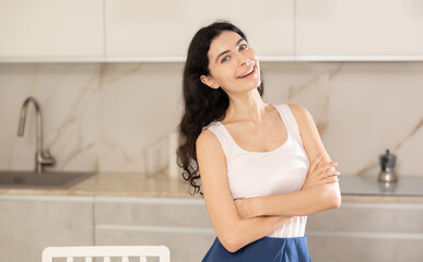 Young positive woman in casual clothes posing in kitchen at home