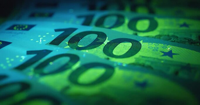 Security signs and elements on euro banknotes glow under ultraviolet light. Green and blue 100 Euro banknotes under UV light. Cinema 4K 60fps video