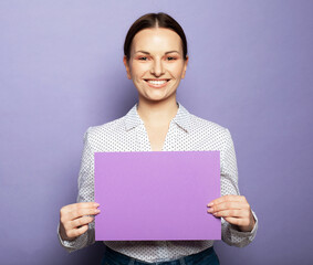 Young woman holding purple blank advertising board standing on lilac background in studio