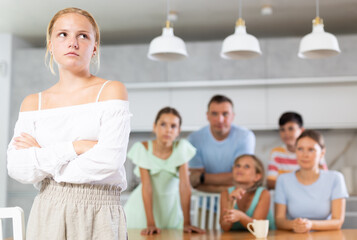 Fototapeta premium Offended girl child has turned back on large family and does not want to talk to household. Parents scolded daughter for inappropriate behavior at school, non-fulfillment of household duties