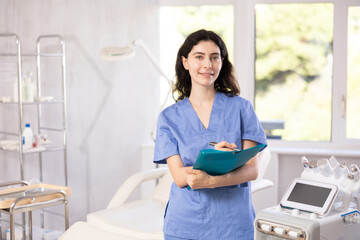 Female cosmetic doctor meticulously stands in her clinic, recording detailed notes in folder, ensuring her patients receive personalized care.