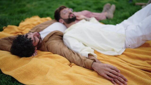 Romantic lgbt couple of guys lying together on blanket, enjoying gently touching each other's hands. Relaxed  gay men have feelings, they talk, male partners like to feel the warmth and care