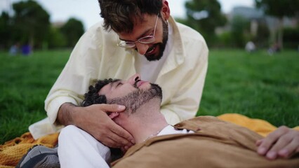 Loving lgbt couple sits in city park while enjoying each other's presence, happy and romantic gay guys kiss and touch each other affectionately, their hearts are filled with love and tenderness.