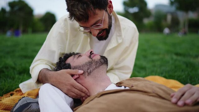 Loving lgbt couple sits in city park while enjoying each other's presence, happy and romantic gay guys kiss and touch each other affectionately, their hearts are filled with love and tenderness.