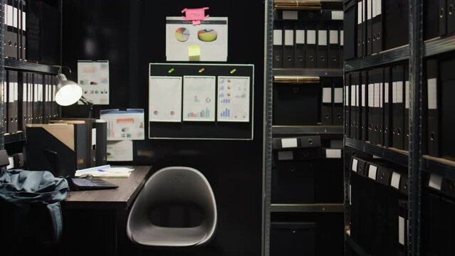 Caucasian policewoman conducts investigative legal work with confidential papers, working on a case. Examining witness statements on laptop, detective cross-references with files from archive shelves.
