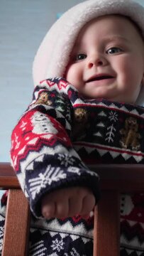 Vertical video, Christmas baby portrait. Cute infant wearing Christmas sweater smiling standing in crib.