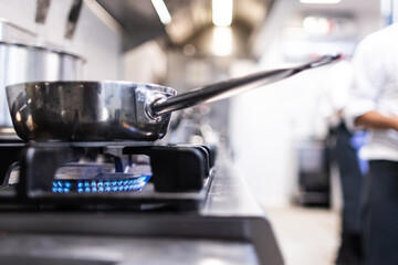 Focused photo of a frying pan on the burning stove of a kitchen - obrazy, fototapety, plakaty
