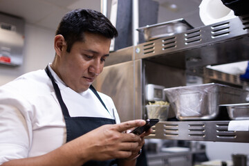 Latin chef looking at his mobile phone while he is at work