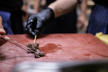 Hand with black glove holding a lamb skewer